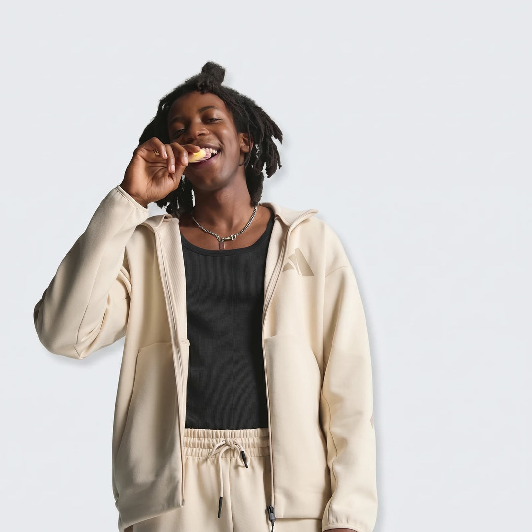 Smiling man with dreadlocks wearing a light beige Adidas Z.N.E. Full-Zip Hoodie and matching sweatpants.