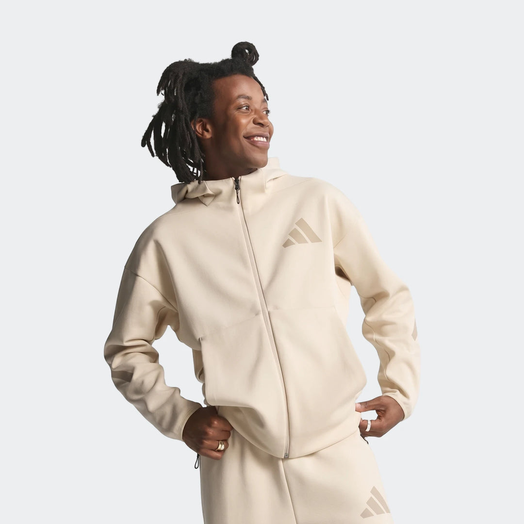 Smiling man wearing a beige Adidas Z.N.E. Full-Zip Hoodie and matching track pants, looking to the right.