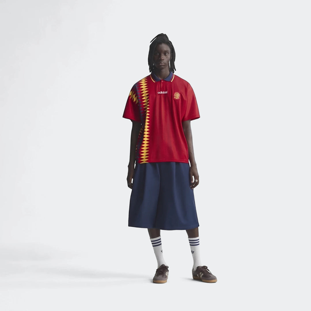 Male model wearing a red Adidas Z.N.E. Track Top with a polo collar, navy culottes, and dark brown sneakers.
