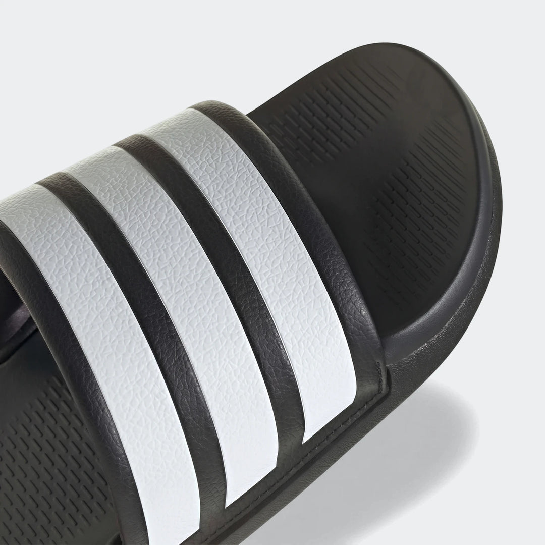 Close-up of a black and white Adidas Adilette Comfort 2.0 slide, showcasing the iconic three white stripes on the strap.