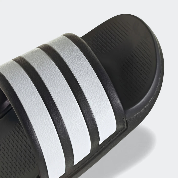 Close-up of a black and white Adidas Adilette Comfort 2.0 slide, showcasing the iconic three white stripes on the strap.