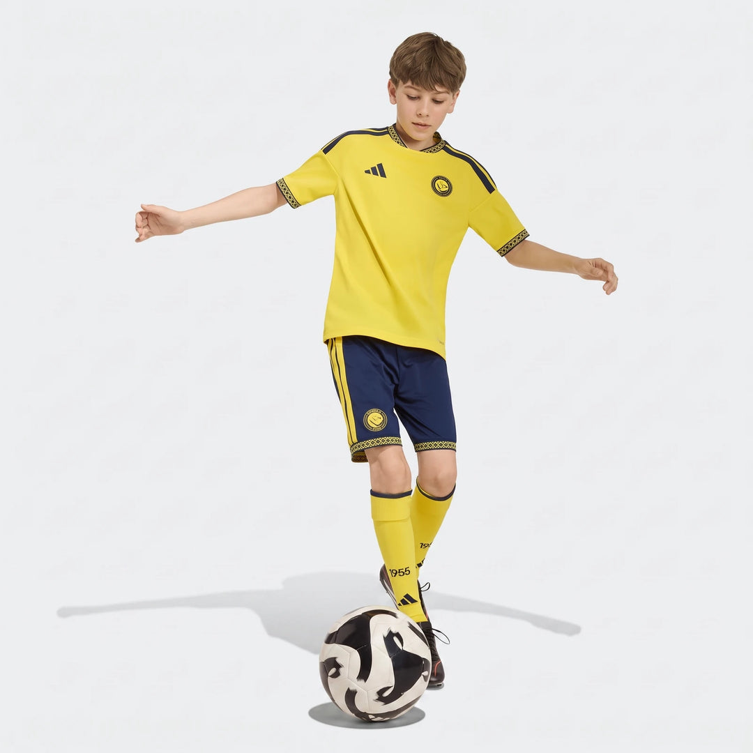 Young boy in yellow and blue Al Nassr FC 26/27 home jersey and shorts balancing a soccer ball.