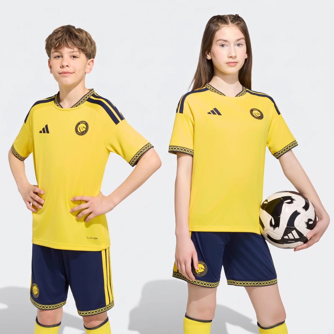 Two kids, a boy and a girl, wear the yellow and navy Al Nassr FC 26/27 Home Jersey soccer uniform with shorts and socks.