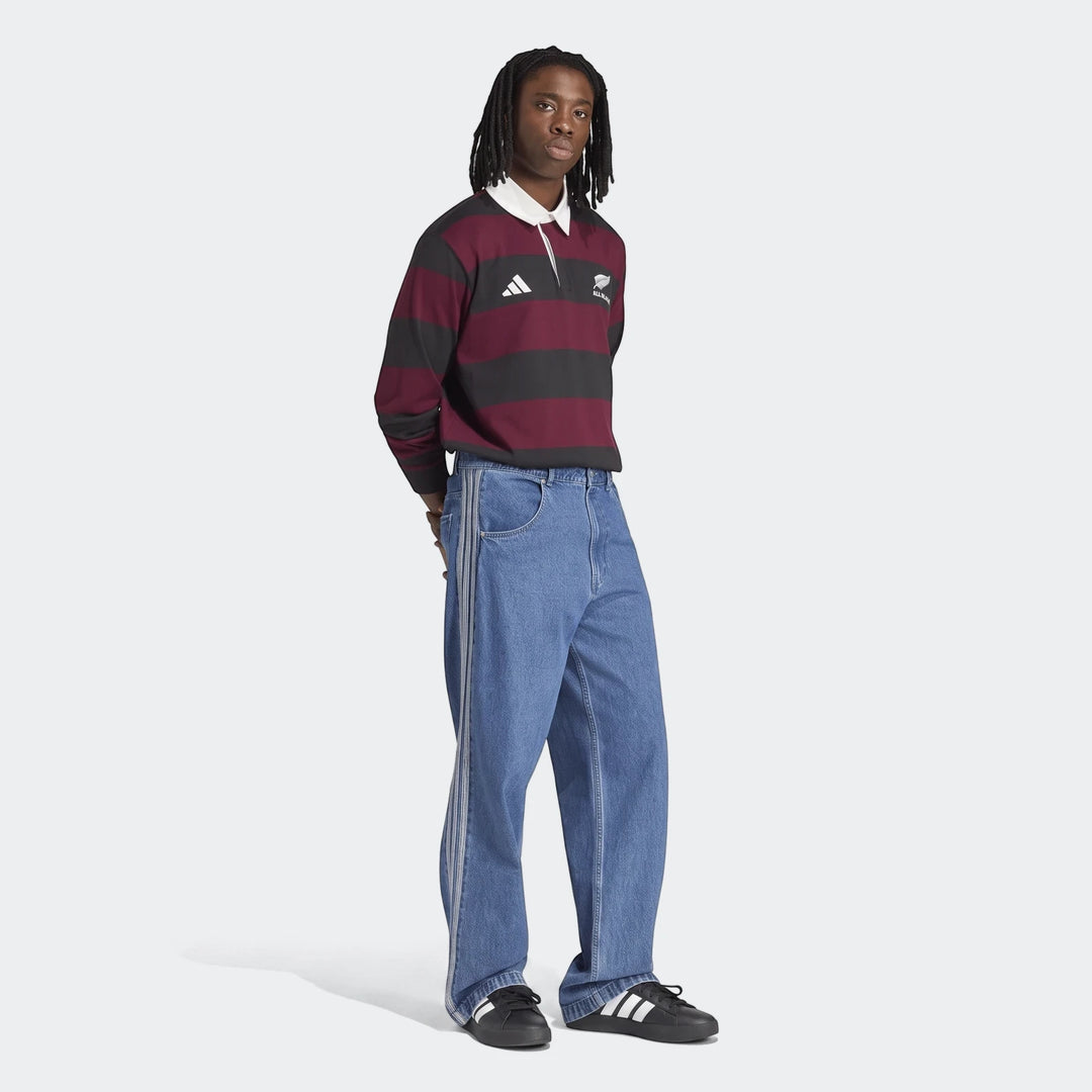 Male model wearing an Adidas All Blacks Heritage long-sleeve rugby polo shirt in burgundy and black stripes.