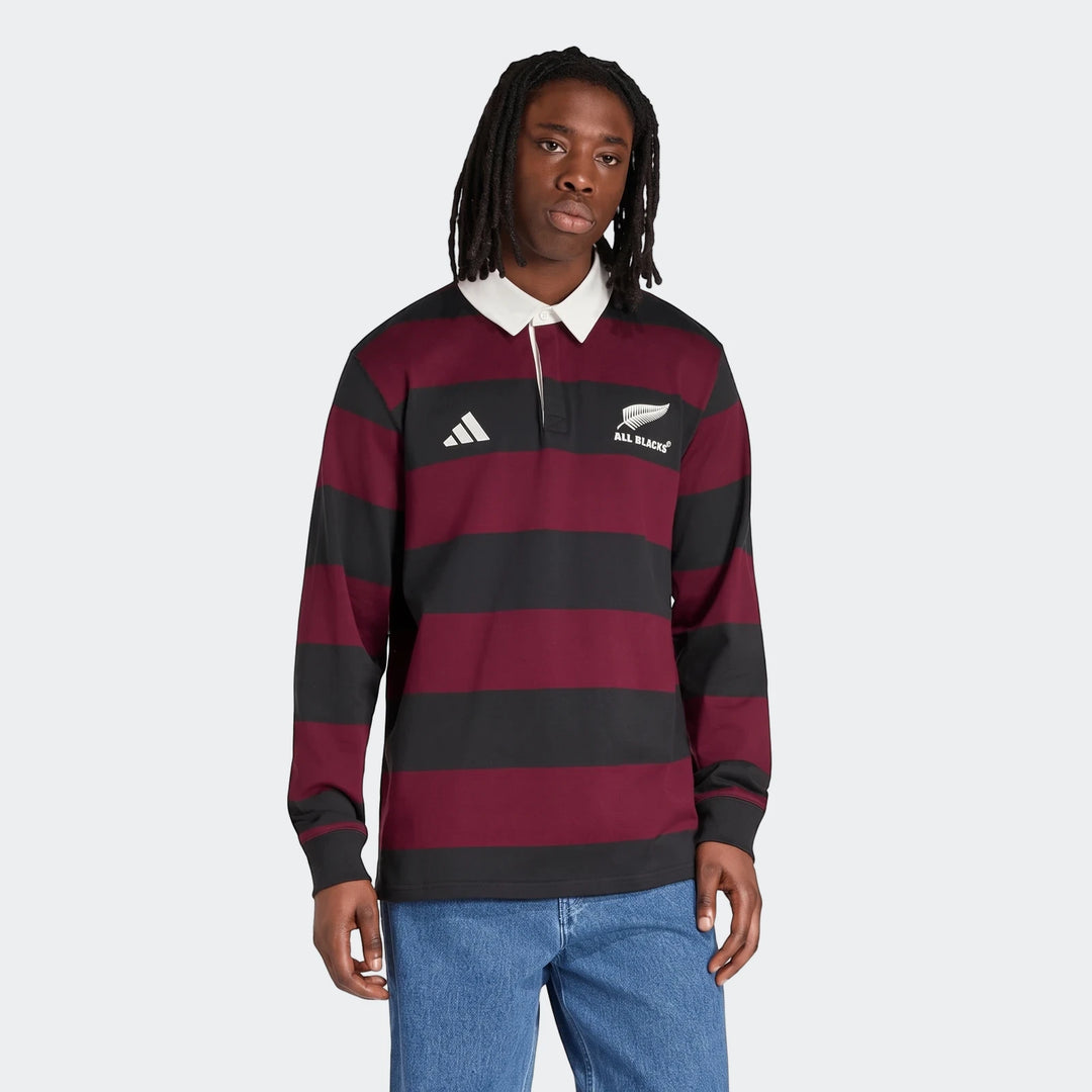 A male model wears an All Blacks Heritage Polo shirt, featuring bold maroon and black horizontal stripes, a white collar,