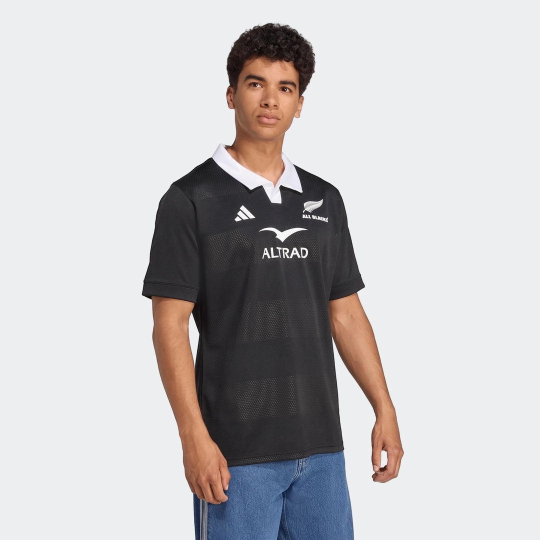 All Blacks Home Jersey worn by a model, black polo-style jersey with white collar, featuring ALTRAD sponsor and fern crest.