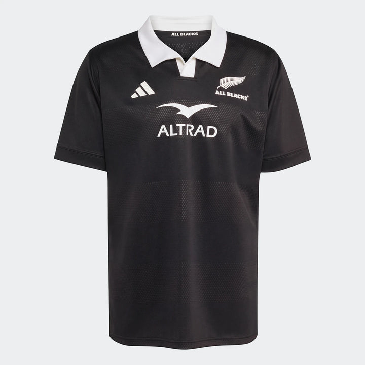 All Blacks Home Jersey in black with white collar, short sleeves, and team logos for rugby fans.