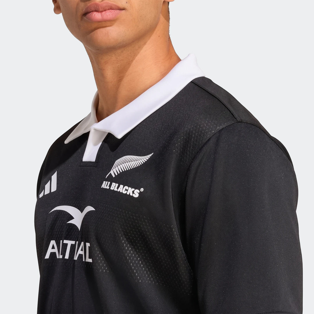Close-up of a black All Blacks Home Jersey with a white collar and fern logo, worn by a person.