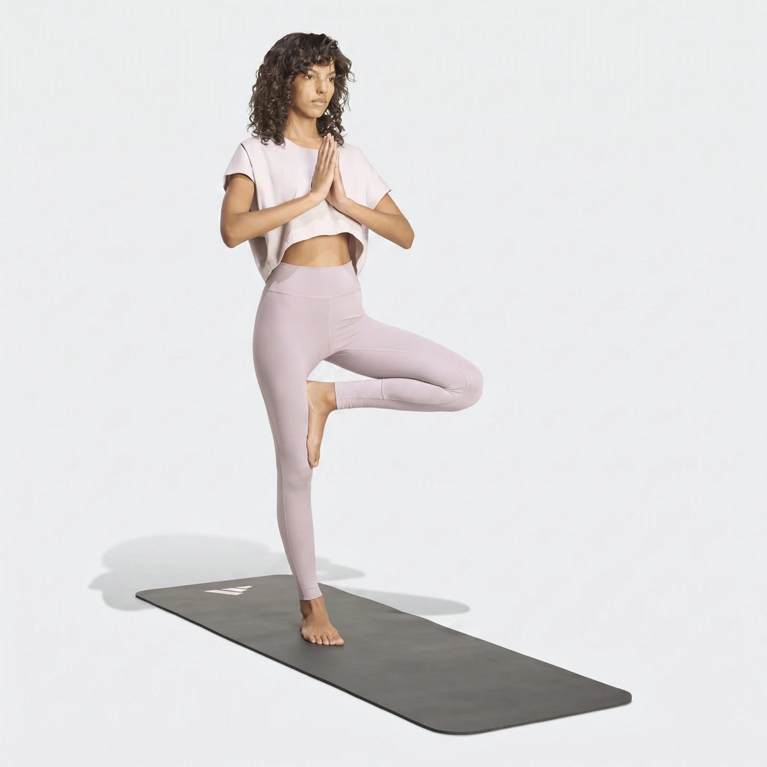 Woman in light purple All Me Essentials Full-Length Tights and a crop top performing a yoga tree pose on a mat.