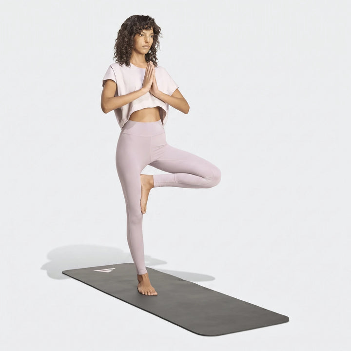 Woman in light purple All Me Essentials Full-Length Tights and a crop top performing a yoga tree pose on a mat.