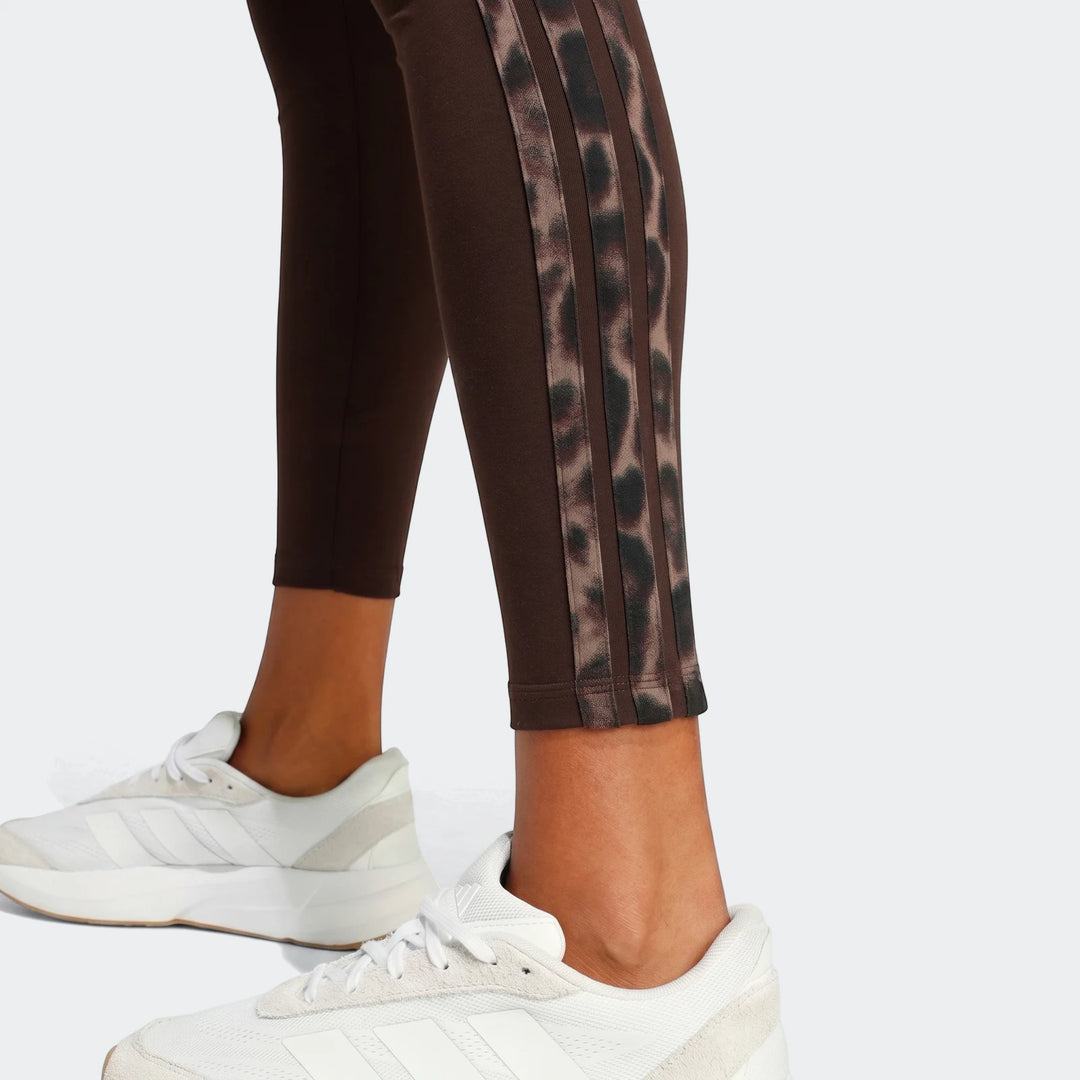 Close-up of brown All-Over Print Infill Leggings with leopard print three stripes, worn by a person with white sneakers.