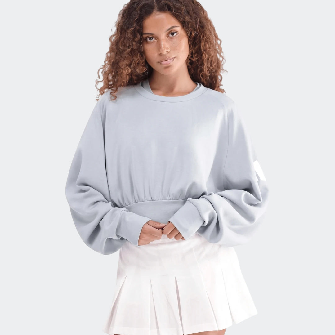 Light blue All Season Slim Sweatshirt on a woman, paired with a white pleated skirt, posing waist-up.