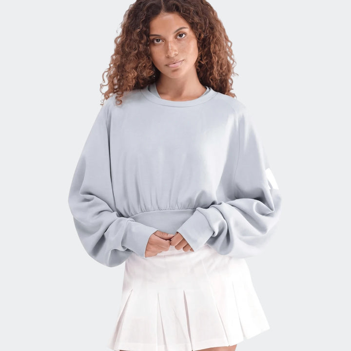Light blue All Season Slim Sweatshirt on a woman, paired with a white pleated skirt, posing waist-up.
