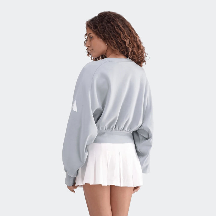 Woman models an All Season Slim Sweatshirt in light blue/gray, featuring loose sleeves and an elasticized waist, paired with