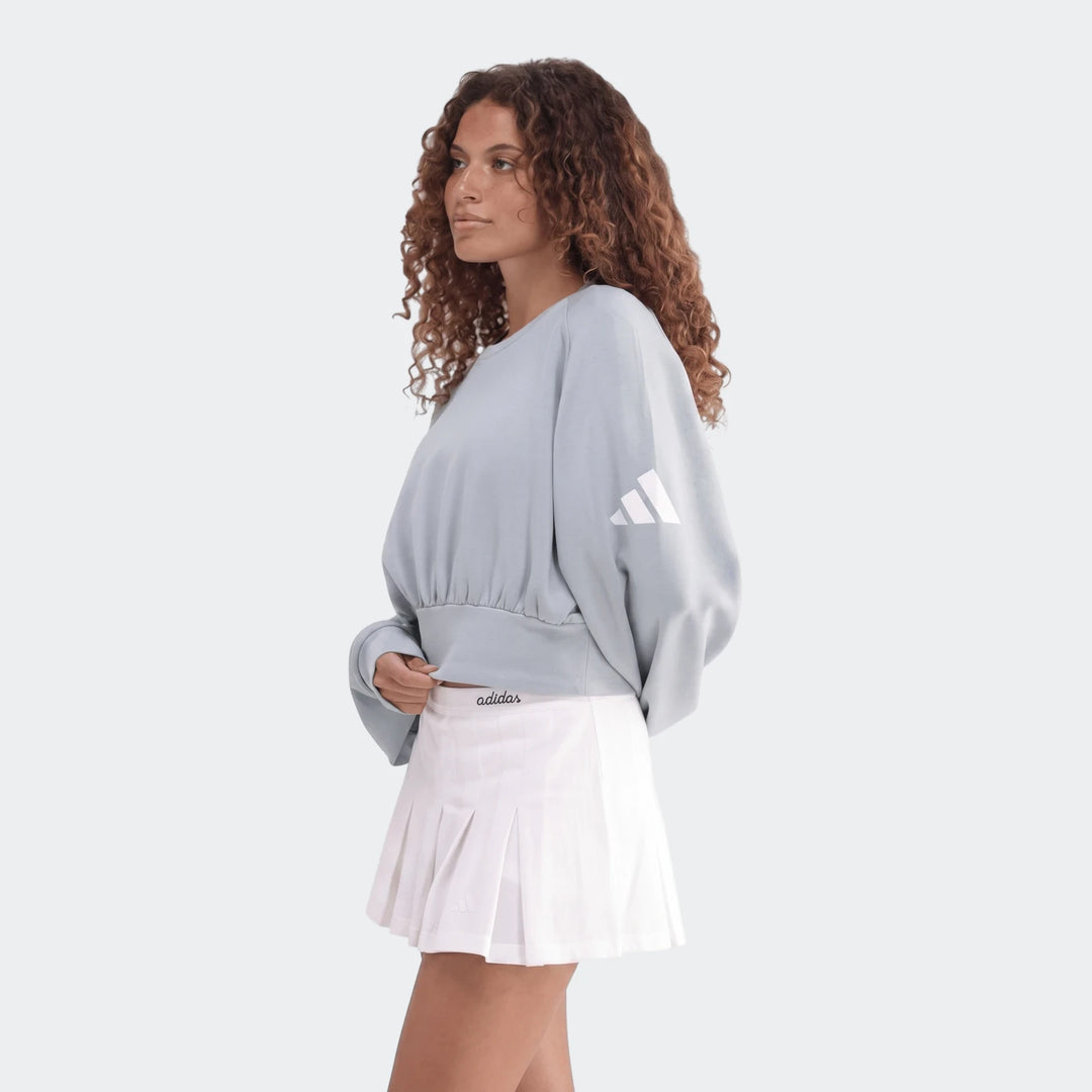 Woman in a light blue All Season Slim Sweatshirt and white pleated skirt, captured in a studio setting.