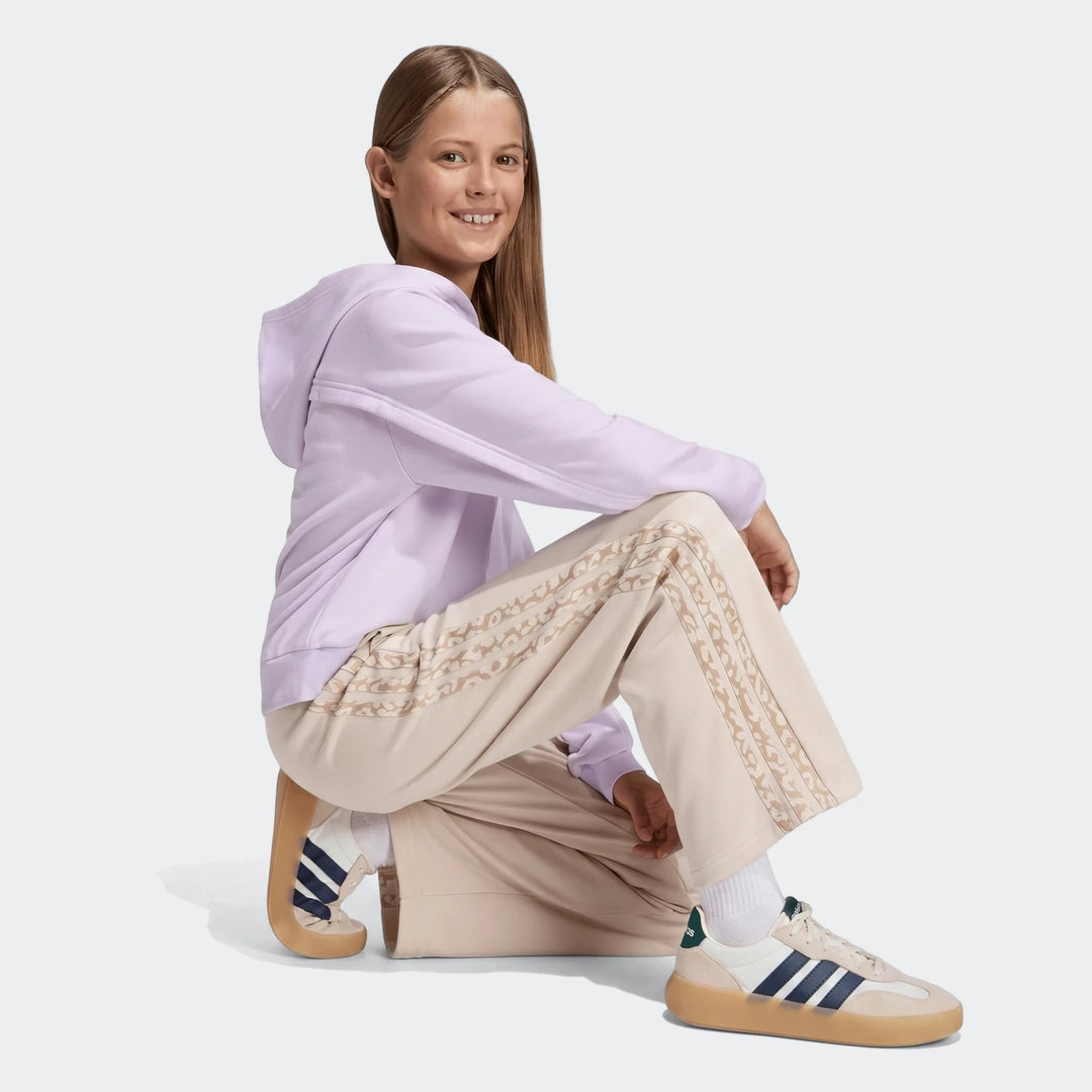 Young girl crouching, wearing beige Angled 3-Stripes French Terry Pants with patterned stripes and a lilac hoodie, full body