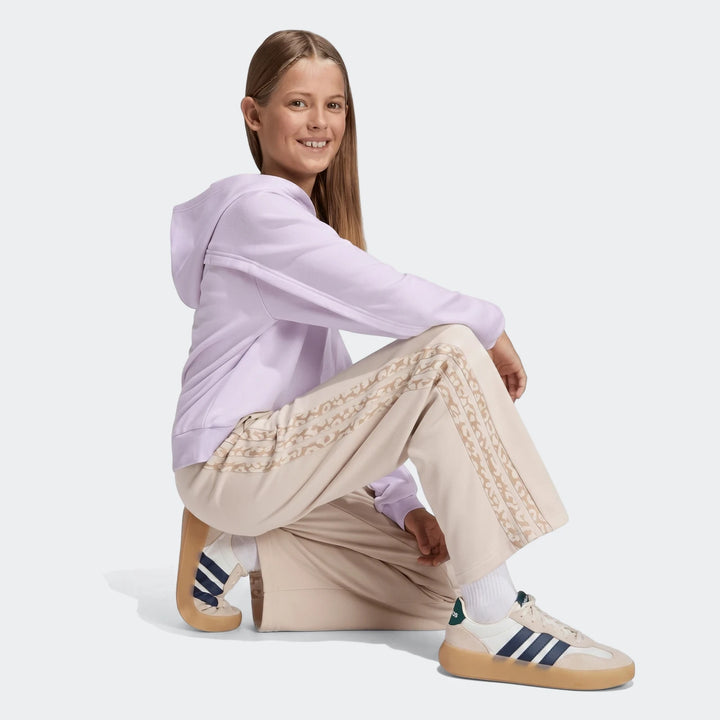 Young girl crouching, wearing beige Angled 3-Stripes French Terry Pants with patterned stripes and a lilac hoodie, full body
