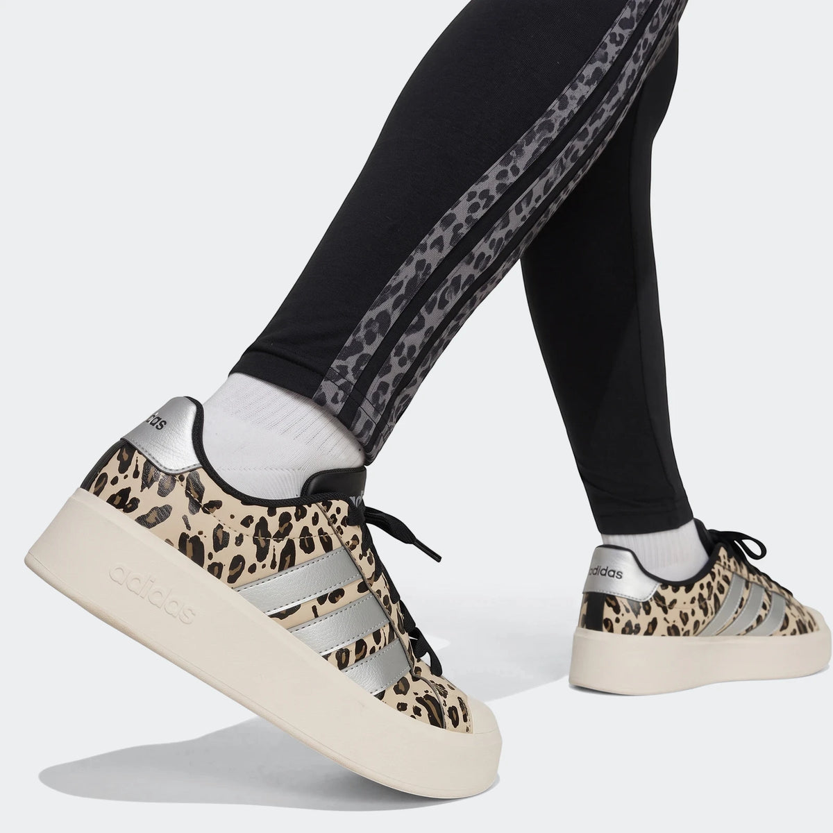 Close-up of a person wearing black Animal Leggings with leopard print stripes and matching leopard print Adidas platform