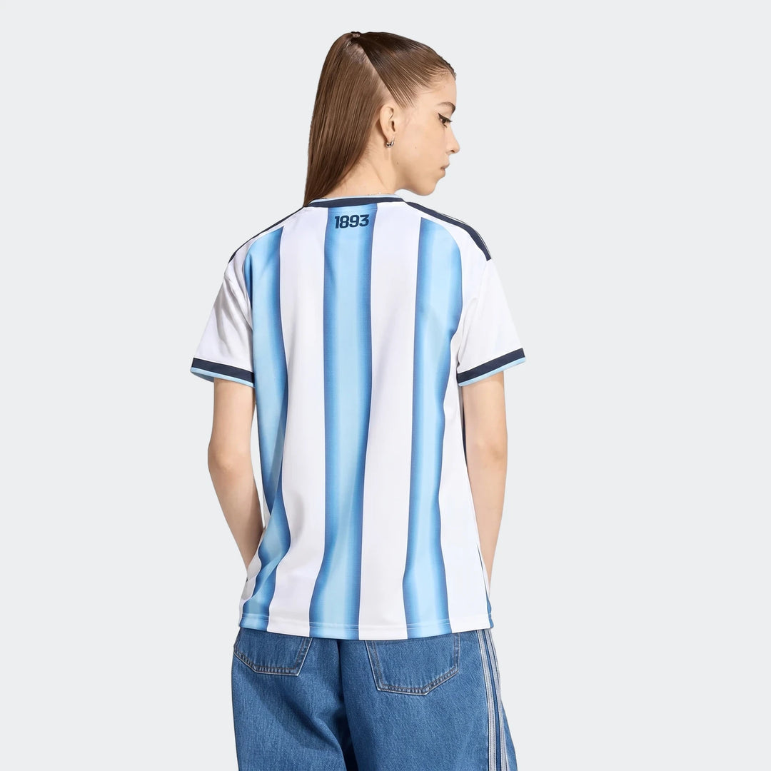 Argentina 26 Home Jersey worn by a female model, shown from the back with blue and white vertical stripes. Model wears blue