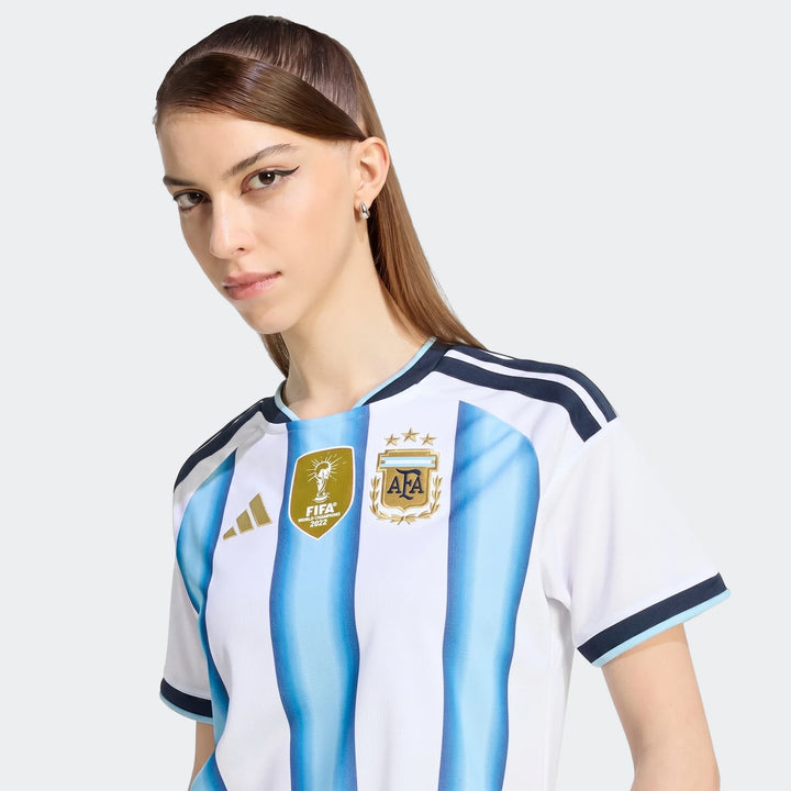 Female model wearing the Argentina 26 Home Jersey, featuring white and light blue vertical stripes with national team logos.
