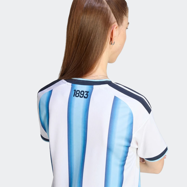 Argentina 26 Home Jersey worn by a woman, back view, showing white and blue stripes with 1893 print.