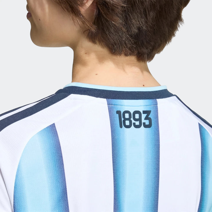 Argentina 26 Home Kids Jersey, back view, on a person with short brown hair. Features light blue and white stripes with
