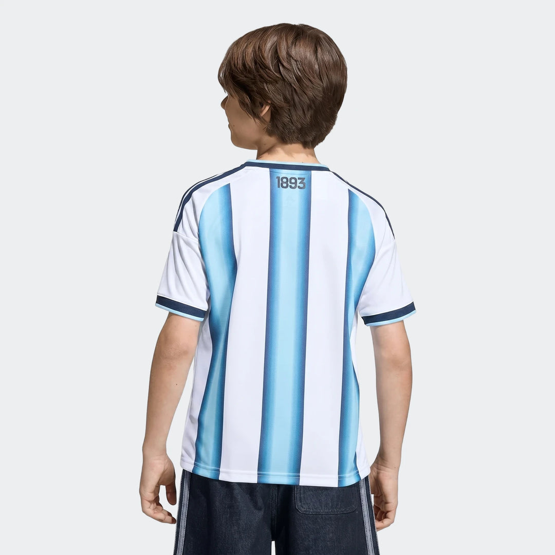 Back view of a young boy wearing the Argentina 26 Home Kids Jersey, featuring white and blue vertical stripes.