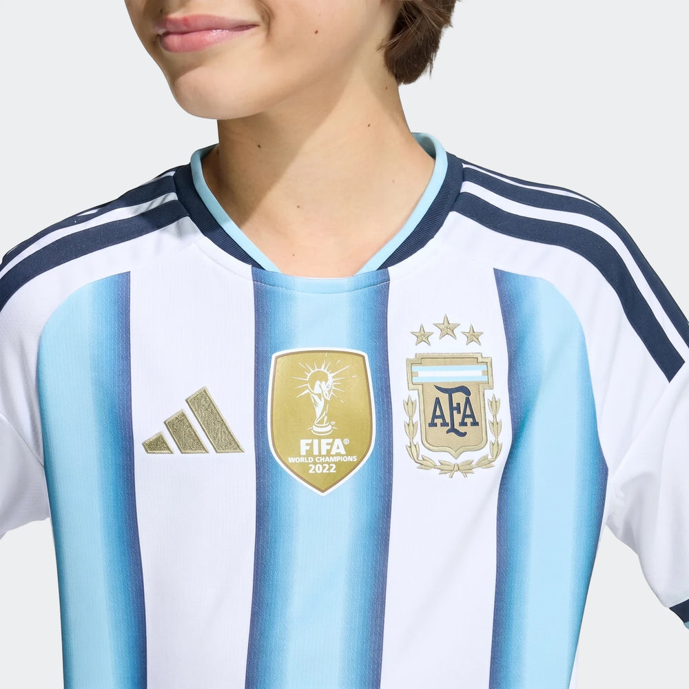 Close-up of a child model wearing the Argentina 26 Home Kids Jersey, featuring white and light blue stripes with Adidas and