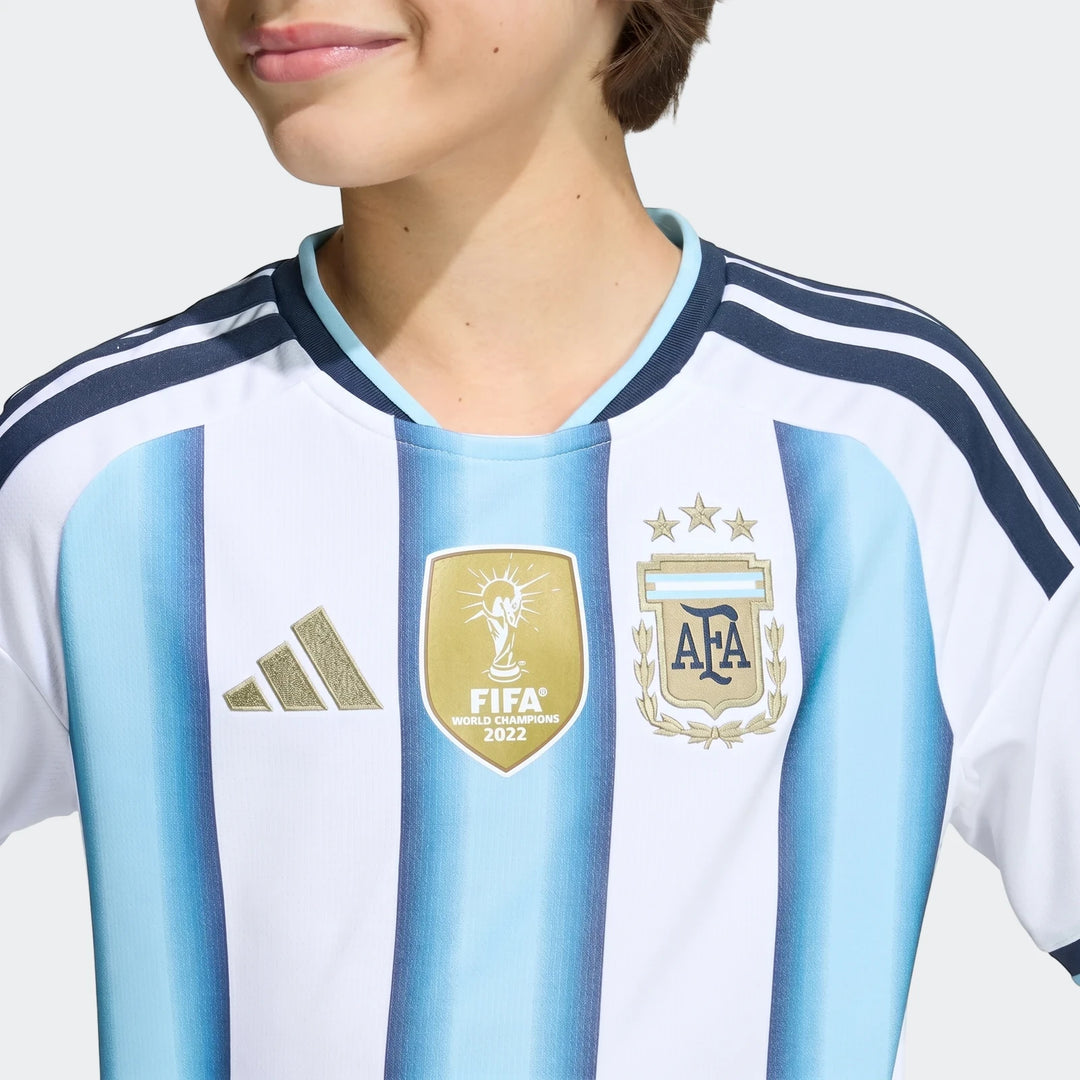 Close-up of a child model wearing the Argentina 26 Home Kids Jersey, featuring white and light blue stripes with Adidas and