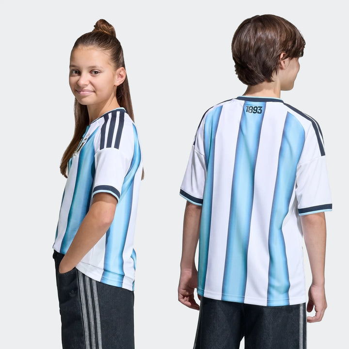 Two kids model the Argentina 26 Home Kids Jersey, featuring white and light blue vertical stripes, shown in front and back