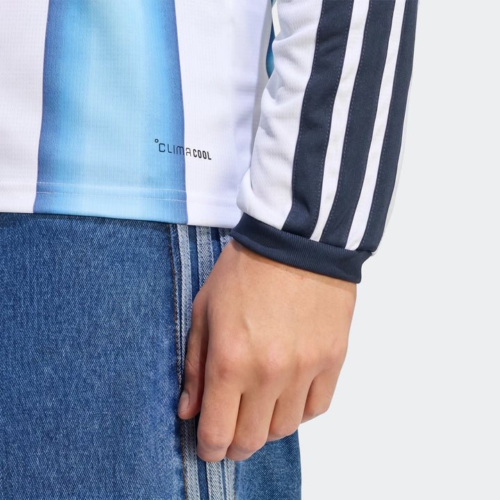 Close-up of a person wearing an Argentina 26 Home Long Sleeve Jersey in blue and white stripes, paired with blue denim jeans.