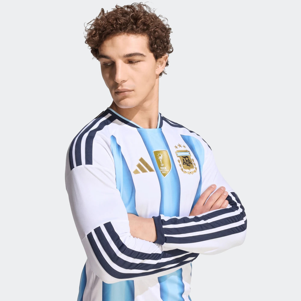 Male model showcasing an Argentina 26 Home Long Sleeve Jersey, featuring white and light blue stripes, with arms crossed.