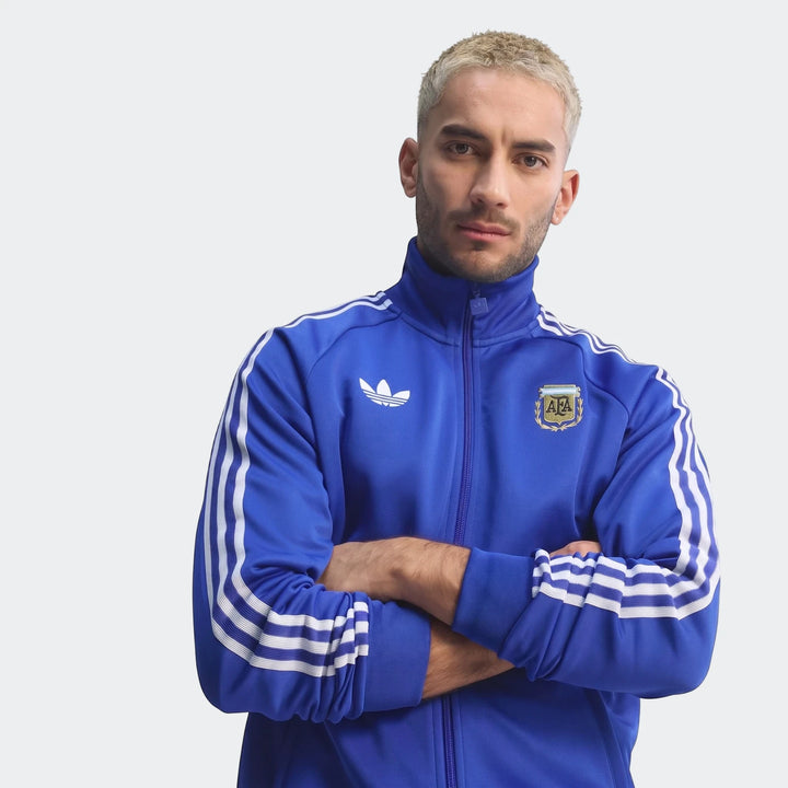 Male model wearing a blue Adidas Argentina Originals track top with white three stripes and AFA crest. Front view.