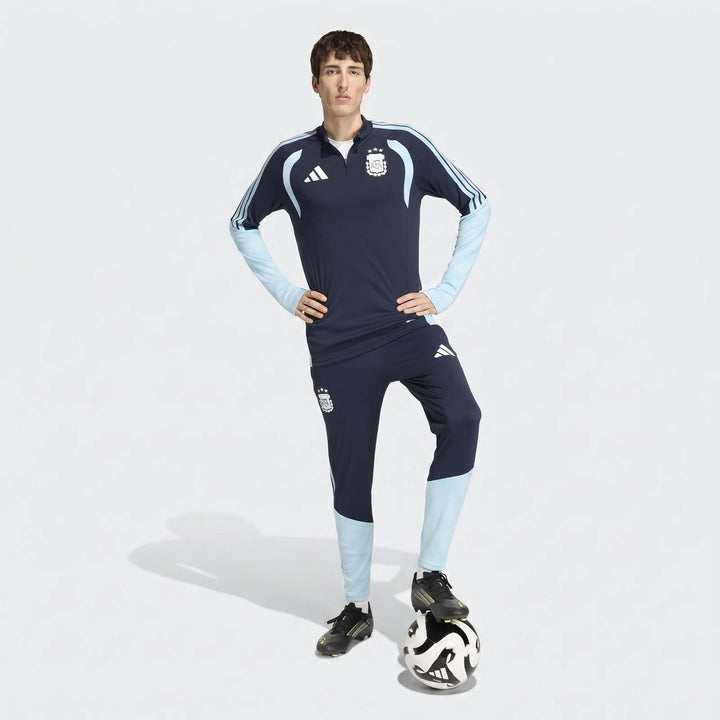 Male model wearing dark blue and light blue Adidas Argentina training pants and matching top, full body shot with a football.