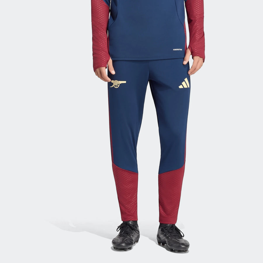 Navy blue and red Arsenal FC 26/27 Cup Tiro training pants with gold logos worn by a person, front view.