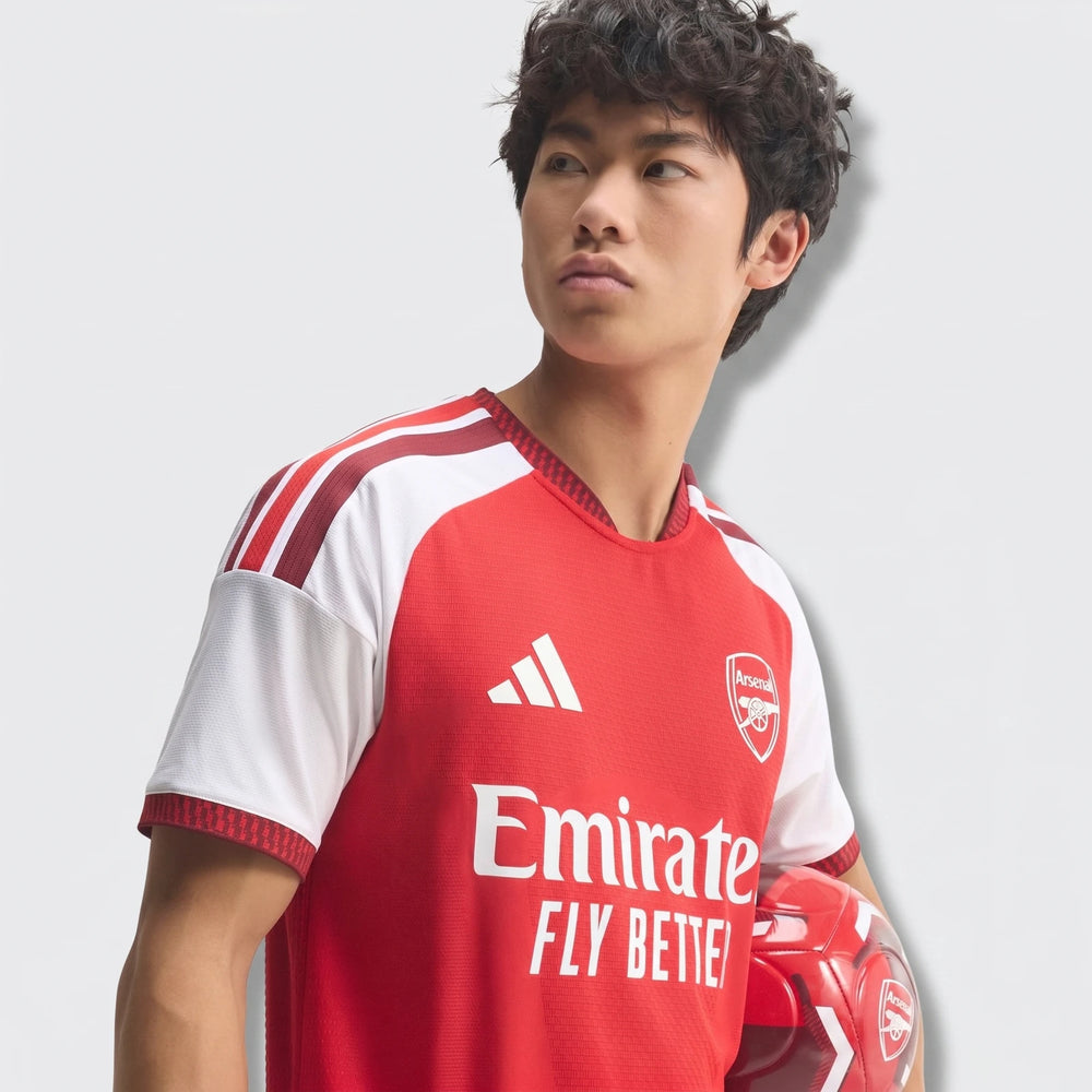 Male model wearing the red and white Arsenal FC 26/27 Home Authentic Jersey, holding a red soccer ball.