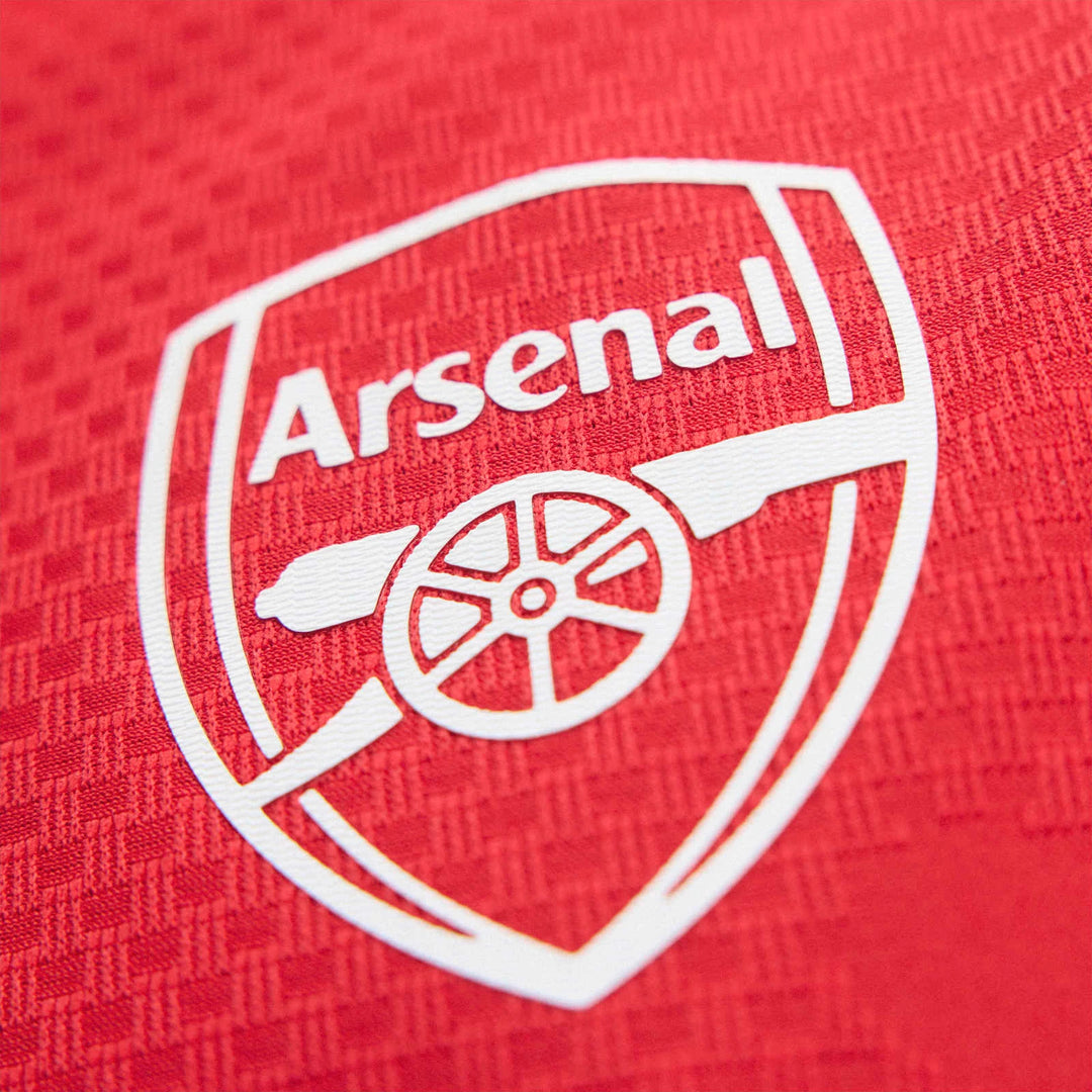 A close-up of a red Arsenal FC 26/27 Home Authentic Jersey, featuring the prominent white Arsenal crest and textured fabric.