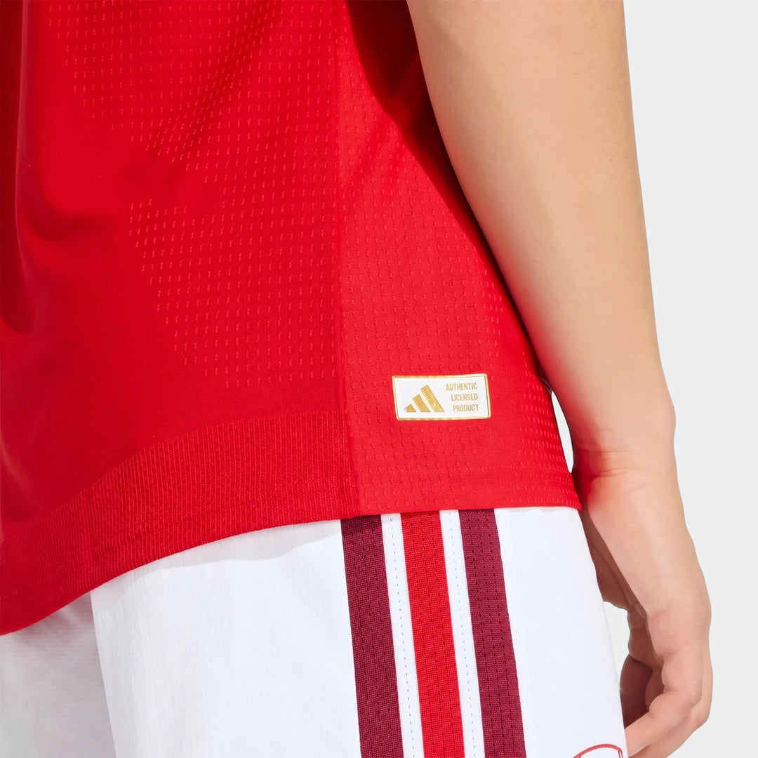 Arsenal Fc 26/27 Home Authentic Jersey in red, worn by a model, featuring textured fabric and a golden Adidas tag, paired
