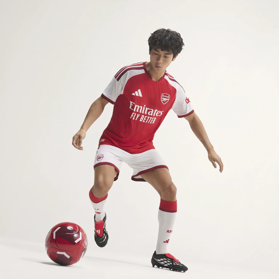 Male model wearing the red and white Arsenal Fc 26/27 Home Authentic Jersey, white shorts, and cleats, playing soccer with a