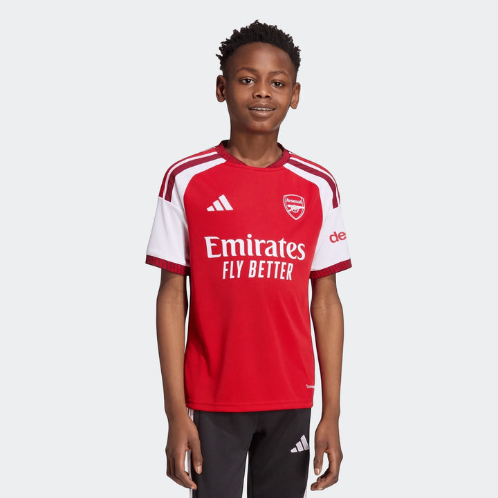 Young boy wearing the red and white Adidas Arsenal FC 26/27 Home Kids Jersey, front view.