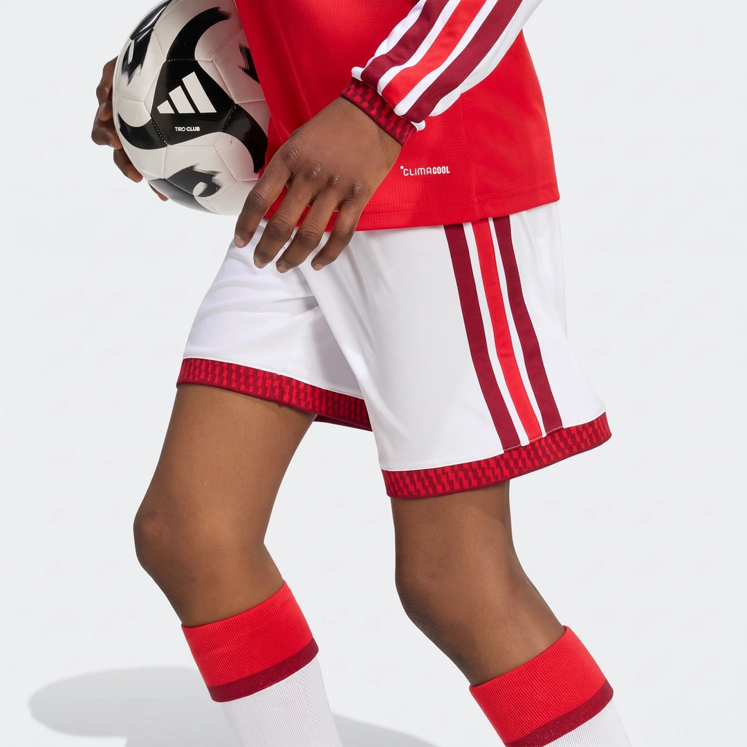 Close-up of a child wearing Arsenal FC 26/27 Home Kids Shorts, white with red and maroon stripes, holding a soccer ball.
