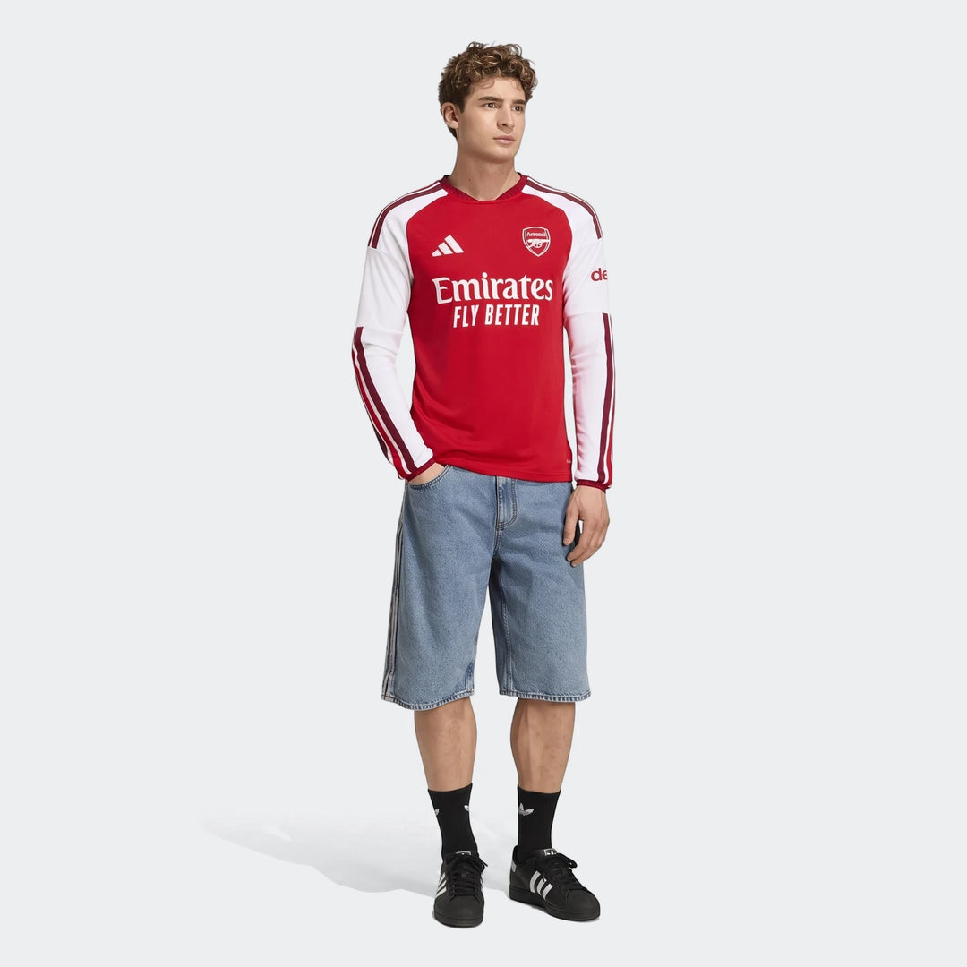 Male model wearing Arsenal Fc 26/27 Home Long Sleeve Jersey in red and white, paired with light blue denim shorts and black