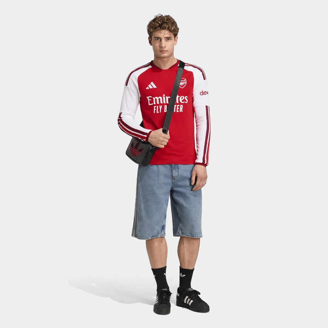 Male model wearing a red and white Adidas Arsenal FC 26/27 Home Long Sleeve Jersey, paired with denim shorts and black