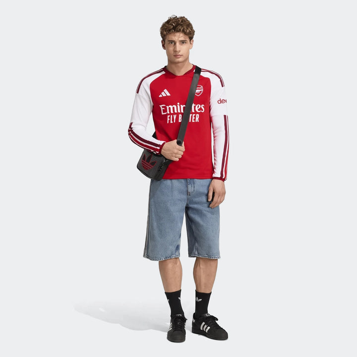 Male model wearing a red and white Adidas Arsenal FC 26/27 Home Long Sleeve Jersey, paired with denim shorts and black