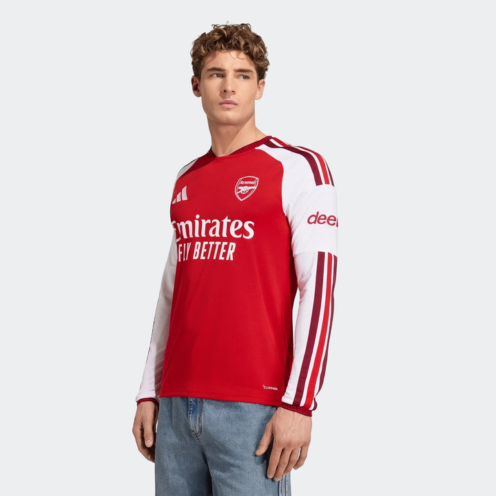 A male model showcases the red and white Arsenal Fc 26/27 Home Long Sleeve Jersey, featuring club crest and sponsor logos.