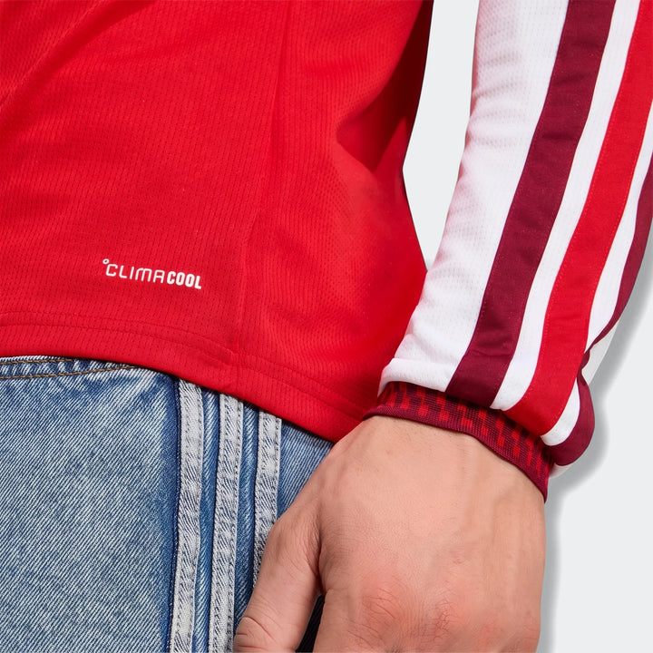 Close-up of a person wearing an Arsenal FC 26/27 Home Long Sleeve Jersey in red with white and maroon stripes and a