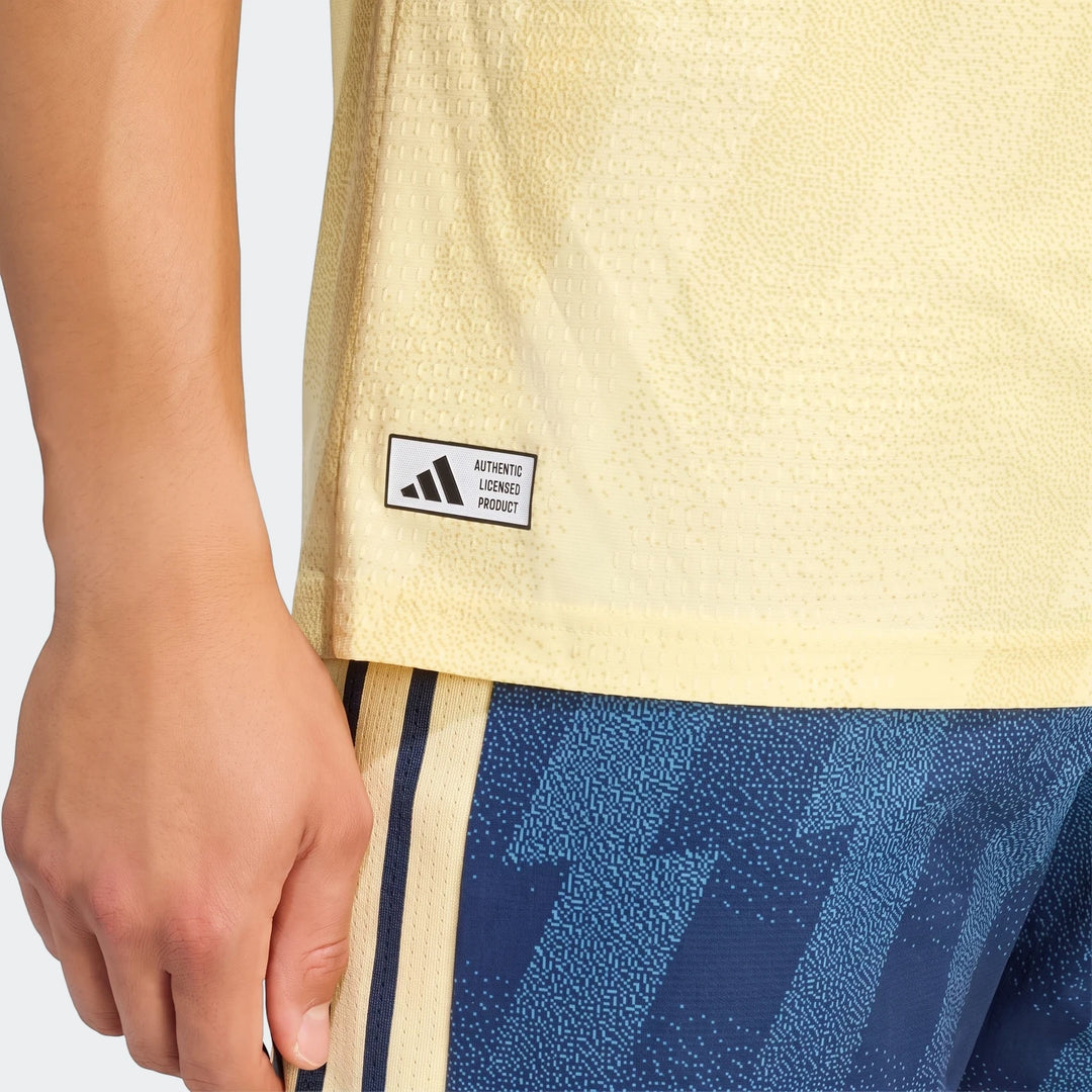 Close-up of a person wearing the yellow Arsenal FC 26/27 Third Authentic Jersey with blue patterned shorts, featuring the