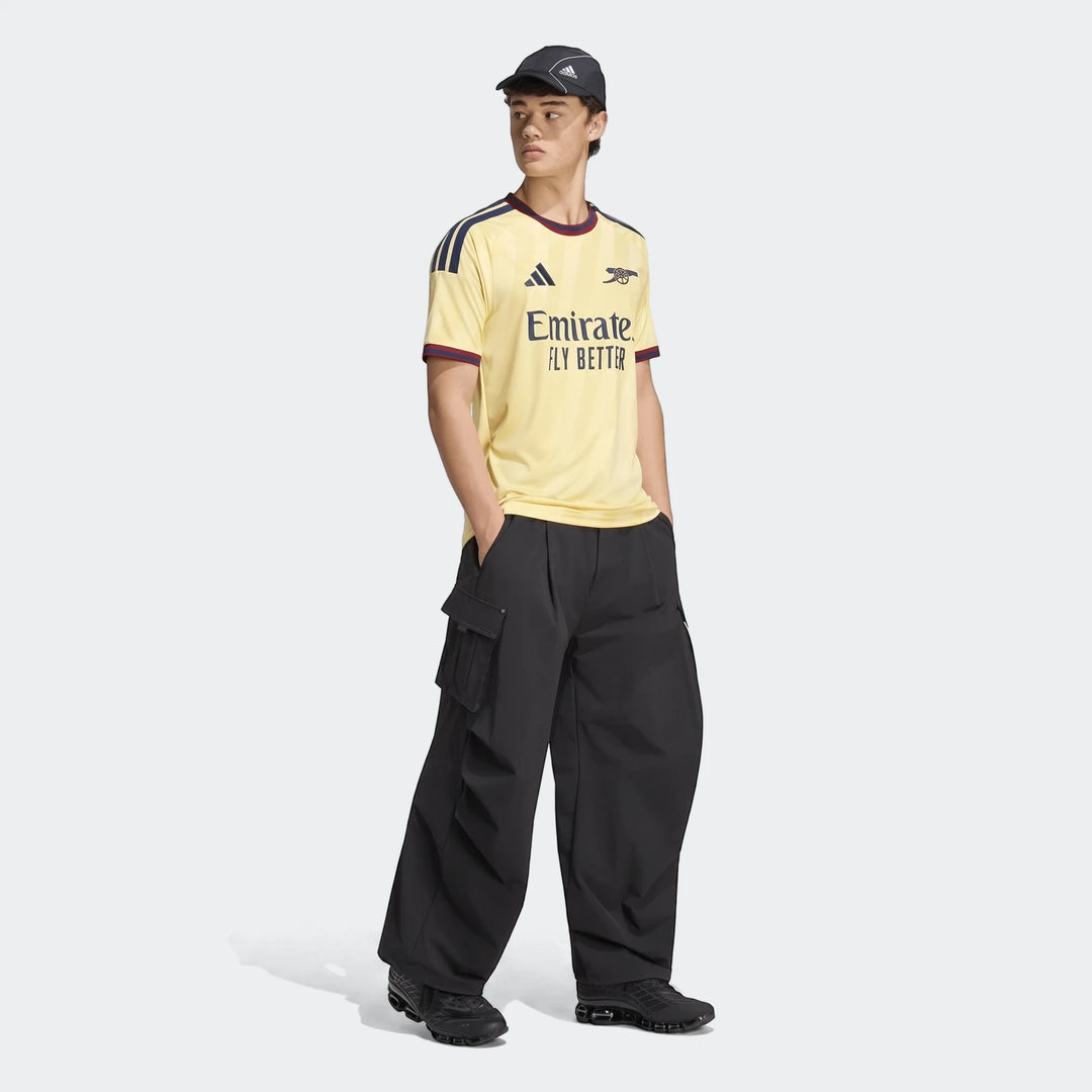 Male model wearing the yellow Adidas Arsenal FC 26/27 Third Jersey with black cargo pants and sneakers, full body shot.