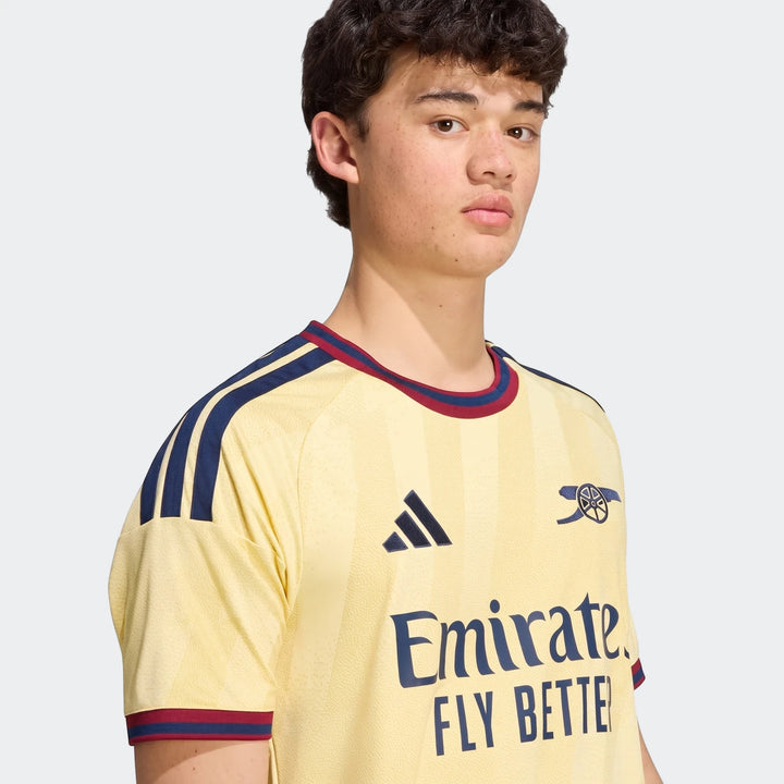 Young man wearing a yellow Adidas Arsenal Fc 26/27 Third Jersey with blue stripes and red trim.