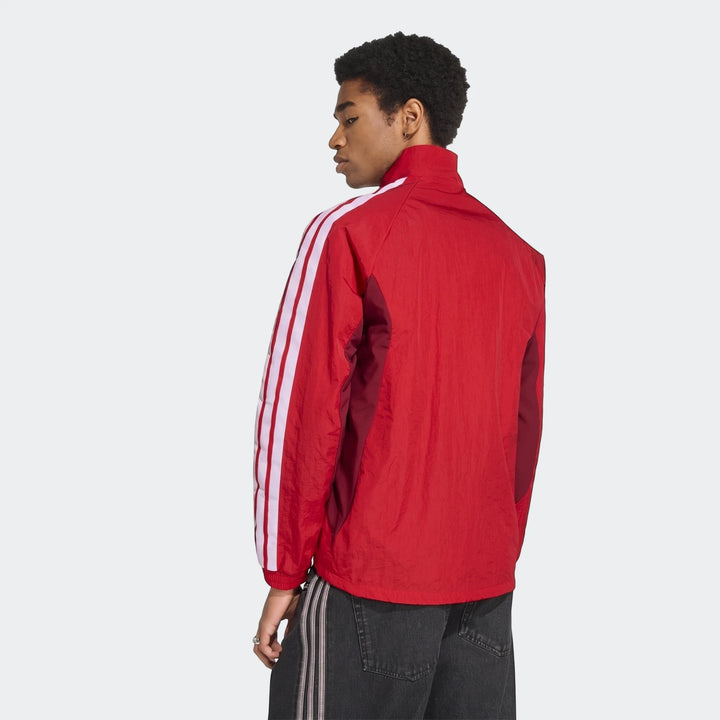 Male model from back-right wearing a red Adidas Arsenal Fc Home Anthem Jacket with white stripes and dark gray jeans.